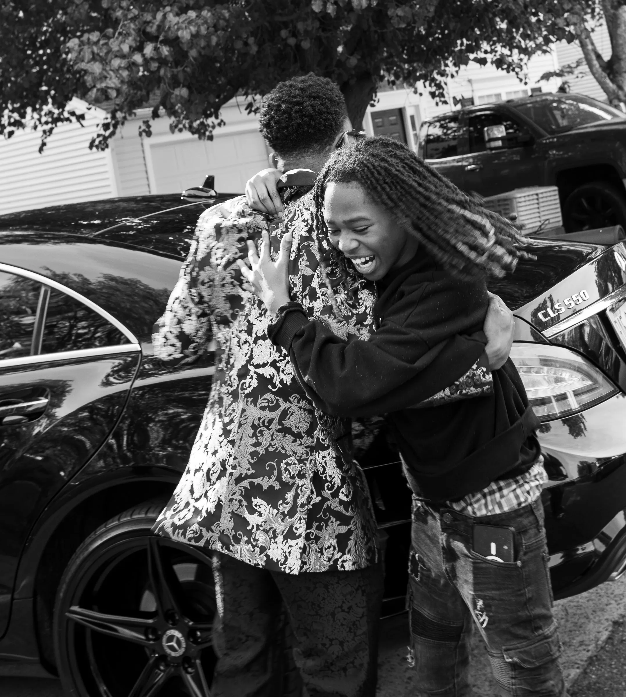 Black and white photograph of him hugging a friend beside a black car