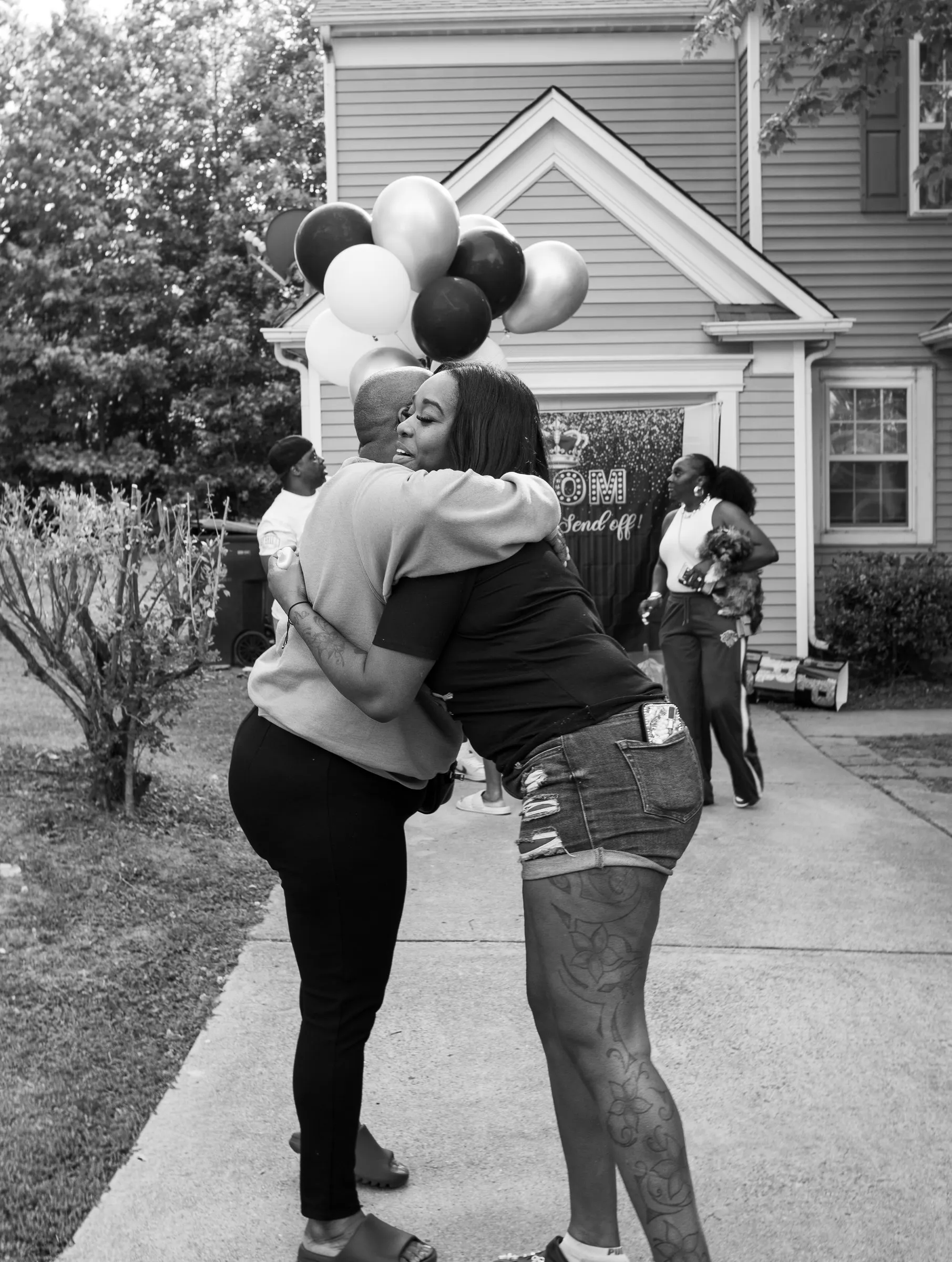 Black and white photograph of a hug on the front walk beside the balloons