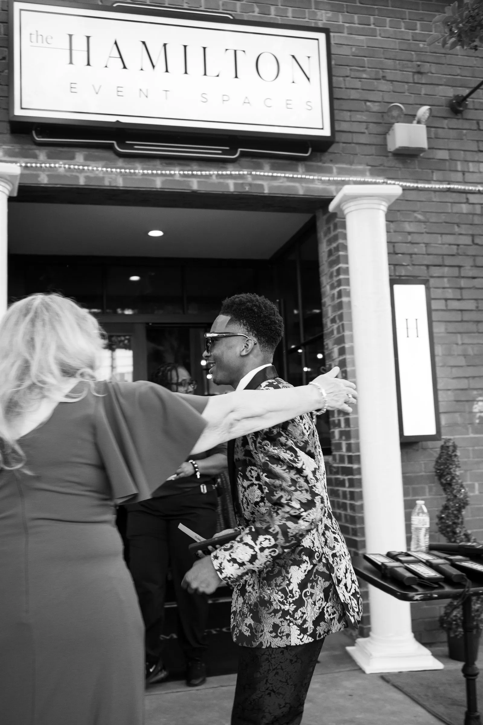 Black and white photograph of him being greeted at the door of The Hamilton