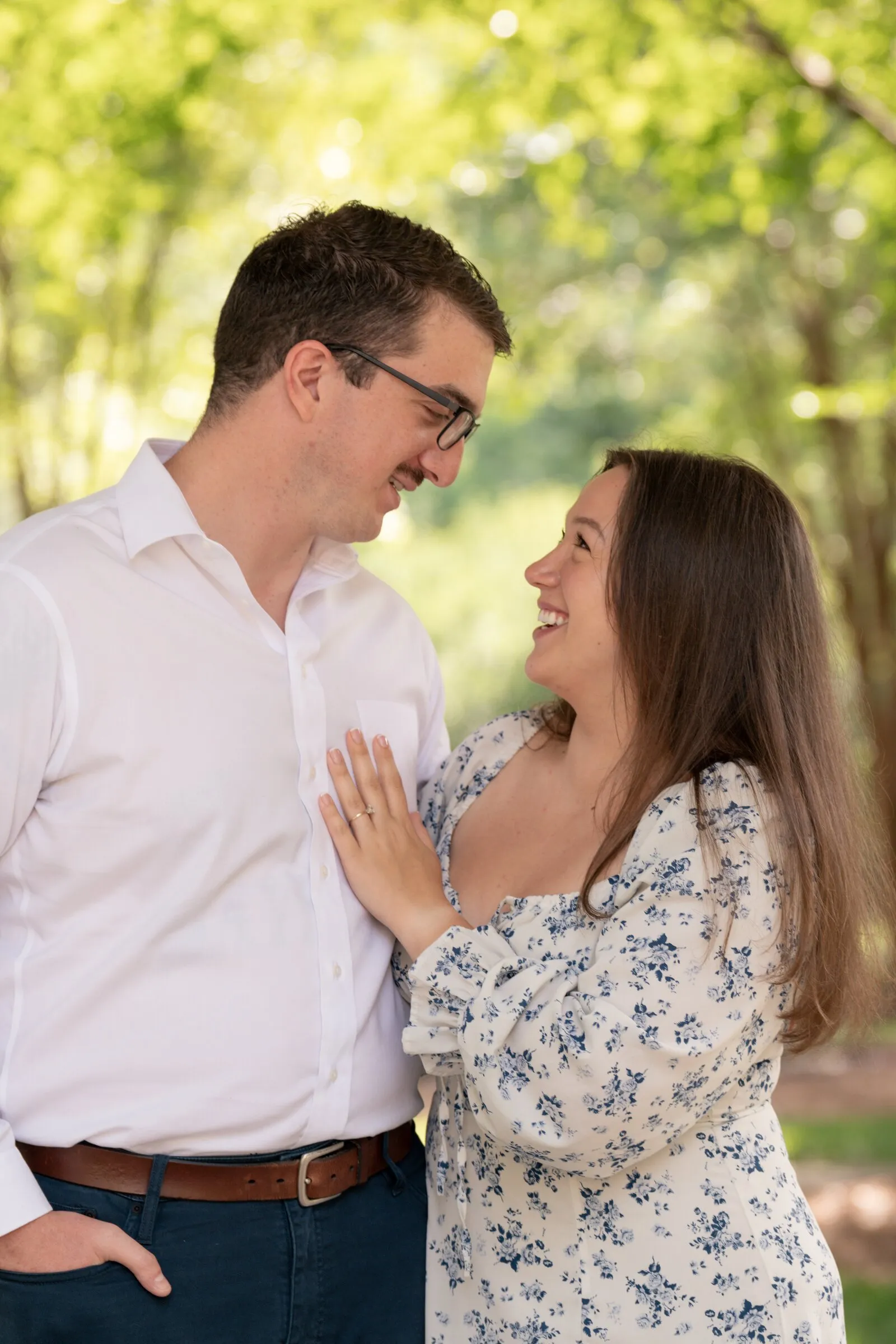 Kayla laughing up at Spencer with her hand on his chest, green trees softly blurred behind them