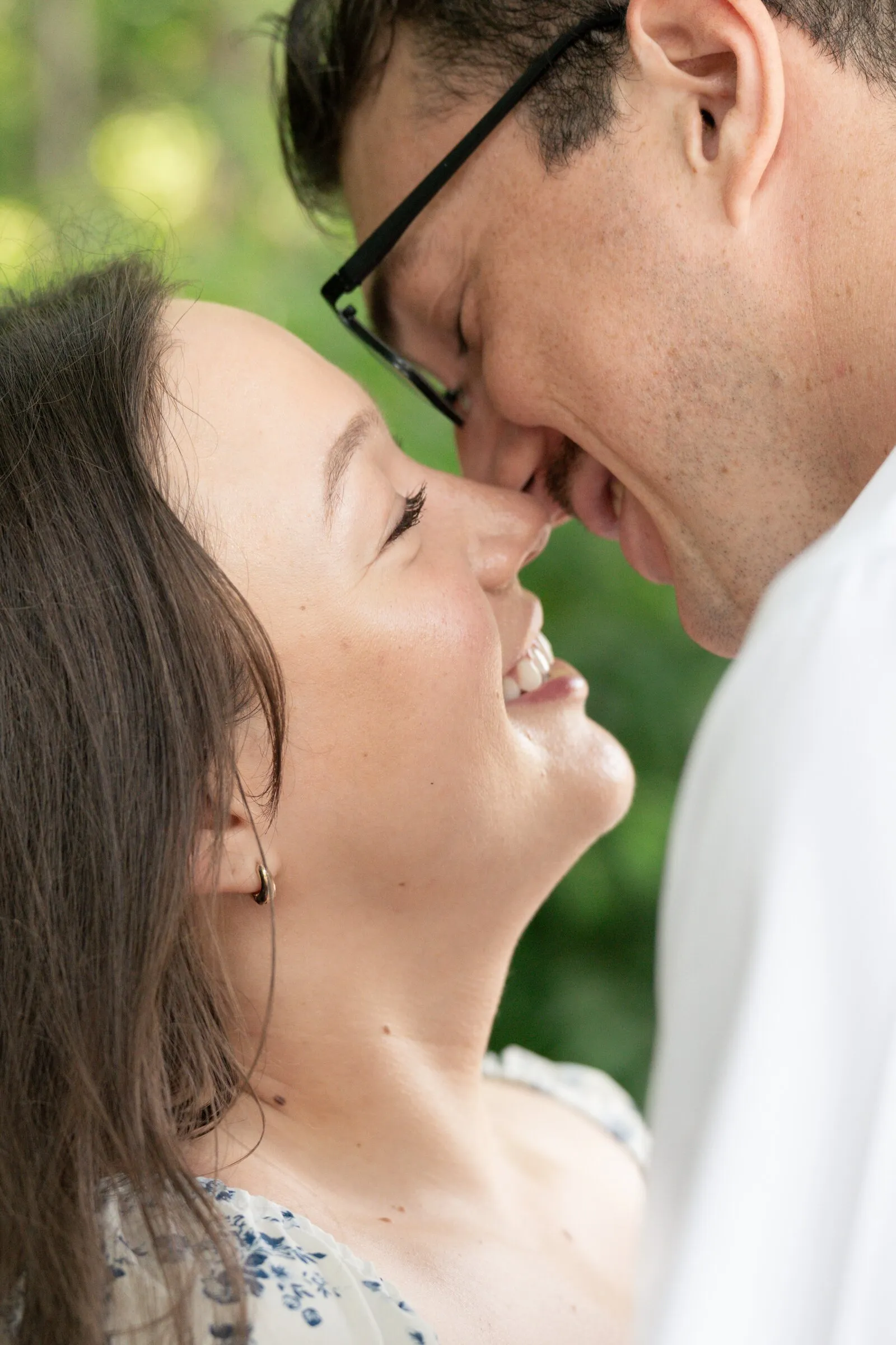 Spencer and Kayla nose to nose and grinning against soft green trees