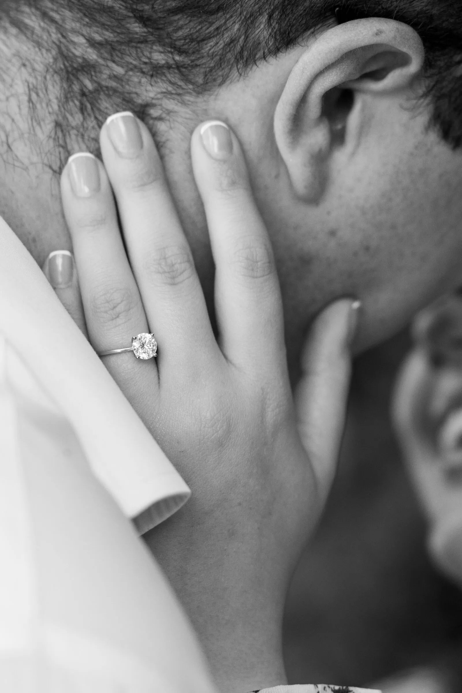 Black and white detail of Kayla's hand and engagement ring resting on Spencer's cheek
