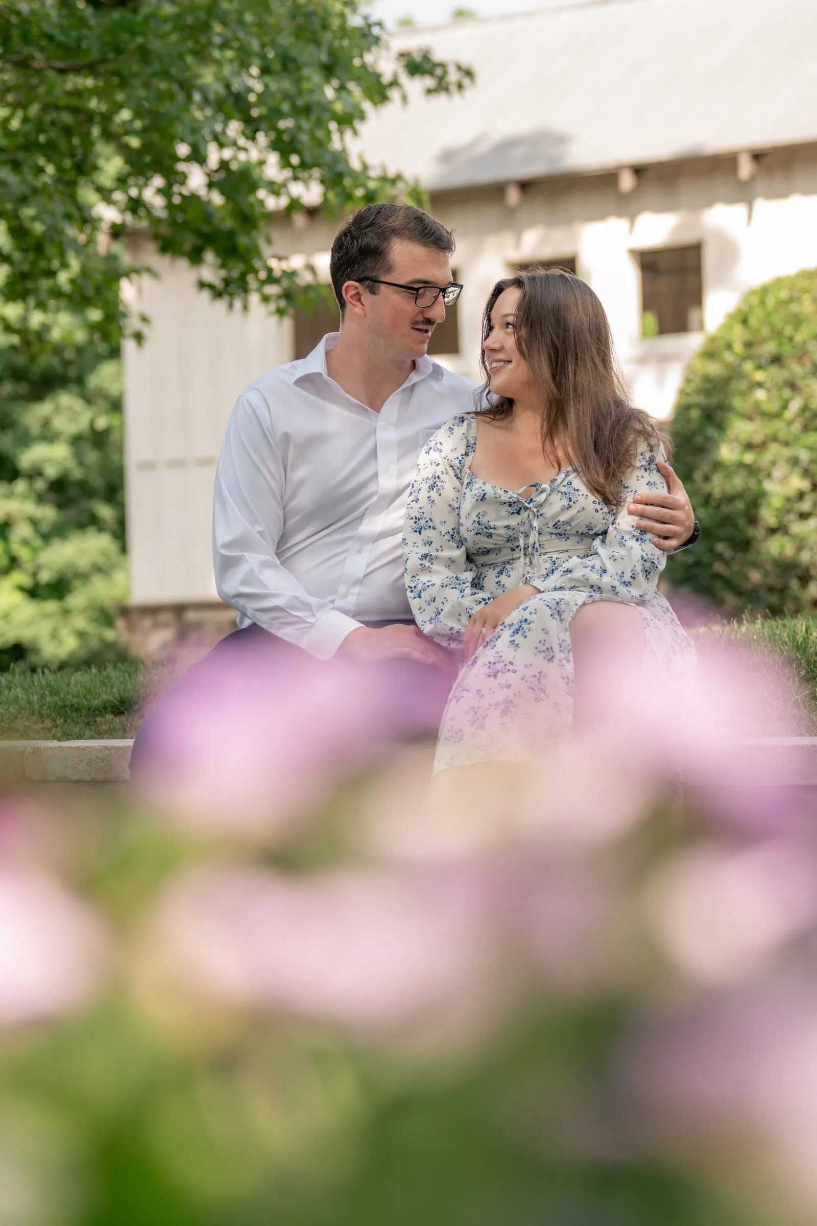 Spencer and Kayla sitting by the mill house, soft pink flowers blurred in the foreground