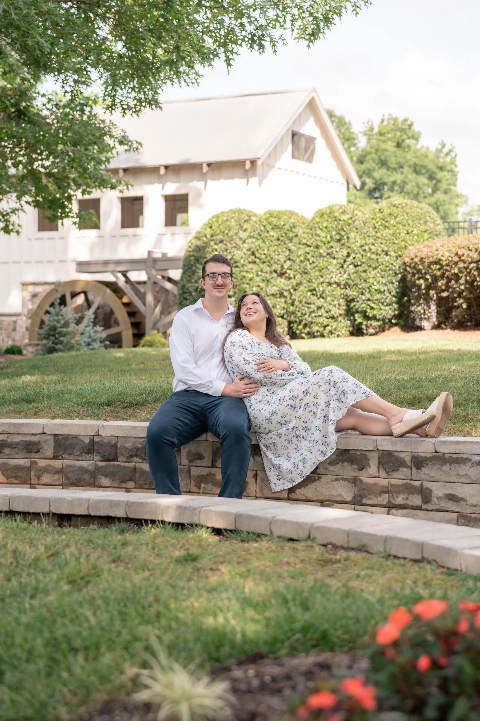Wide view of Spencer and Kayla on the curved stone wall below the Millbridge mill house