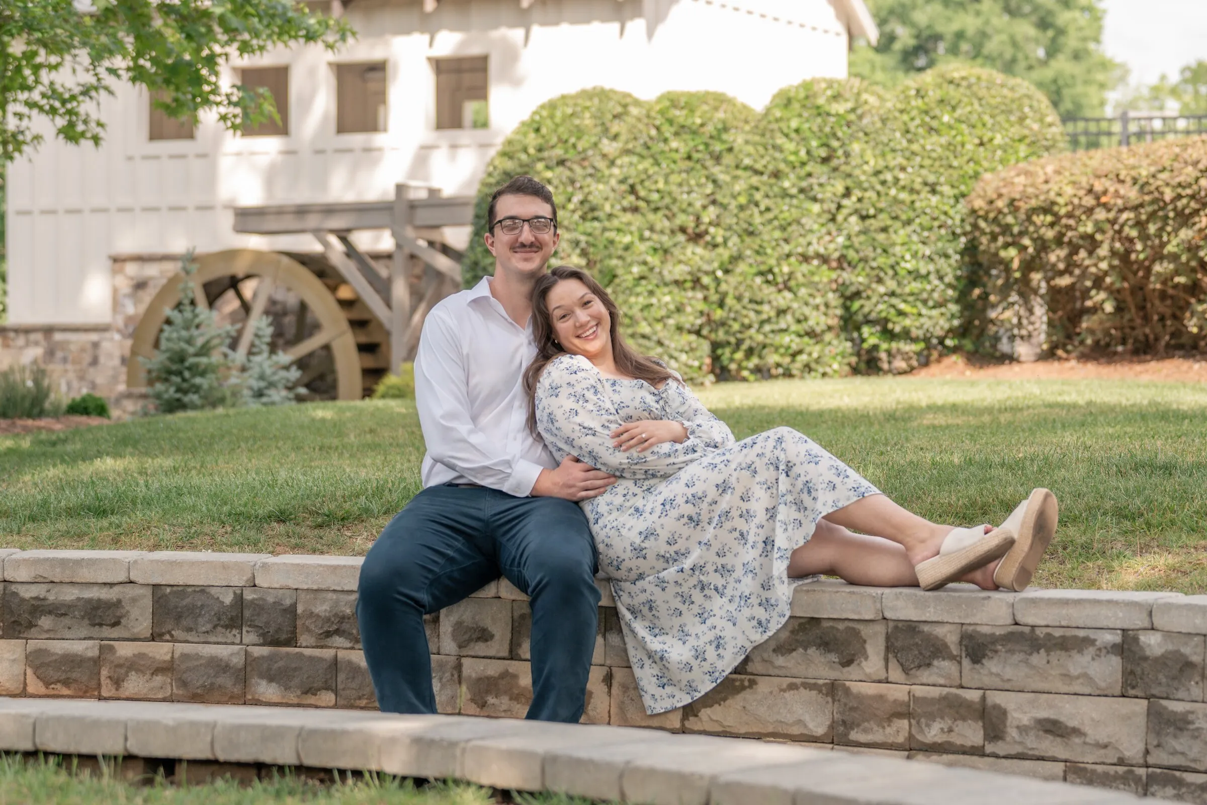 Spencer and Kayla relaxing on the stone wall with the mill's waterwheel and hedges behind them