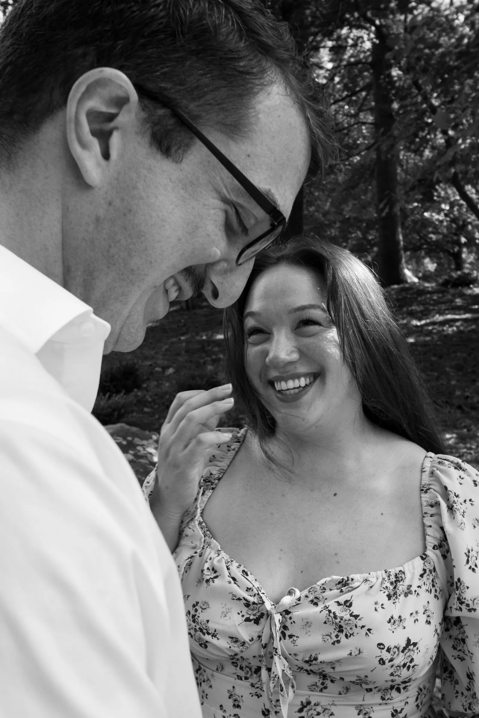 Black and white photograph of Kayla laughing as Spencer leans his head toward hers