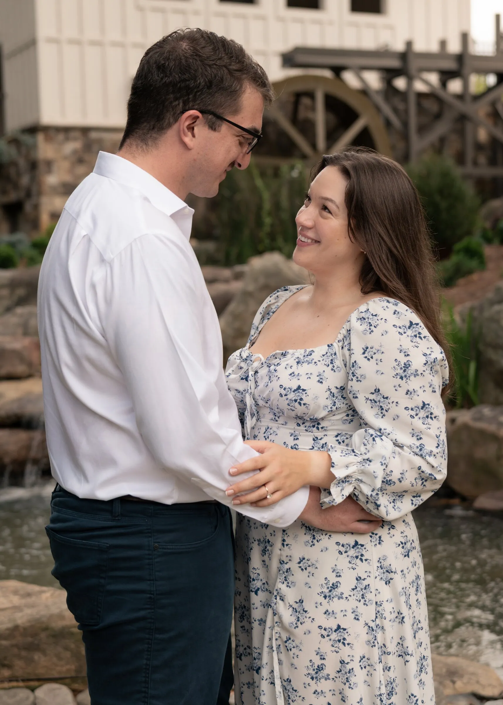 Spencer and Kayla holding each other beside the waterfall, the mill and its waterwheel behind them
