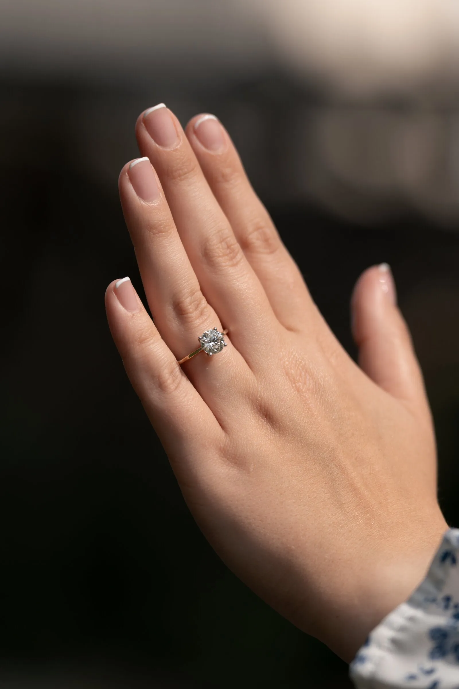 Kayla's raised hand and solitaire engagement ring against a dark background