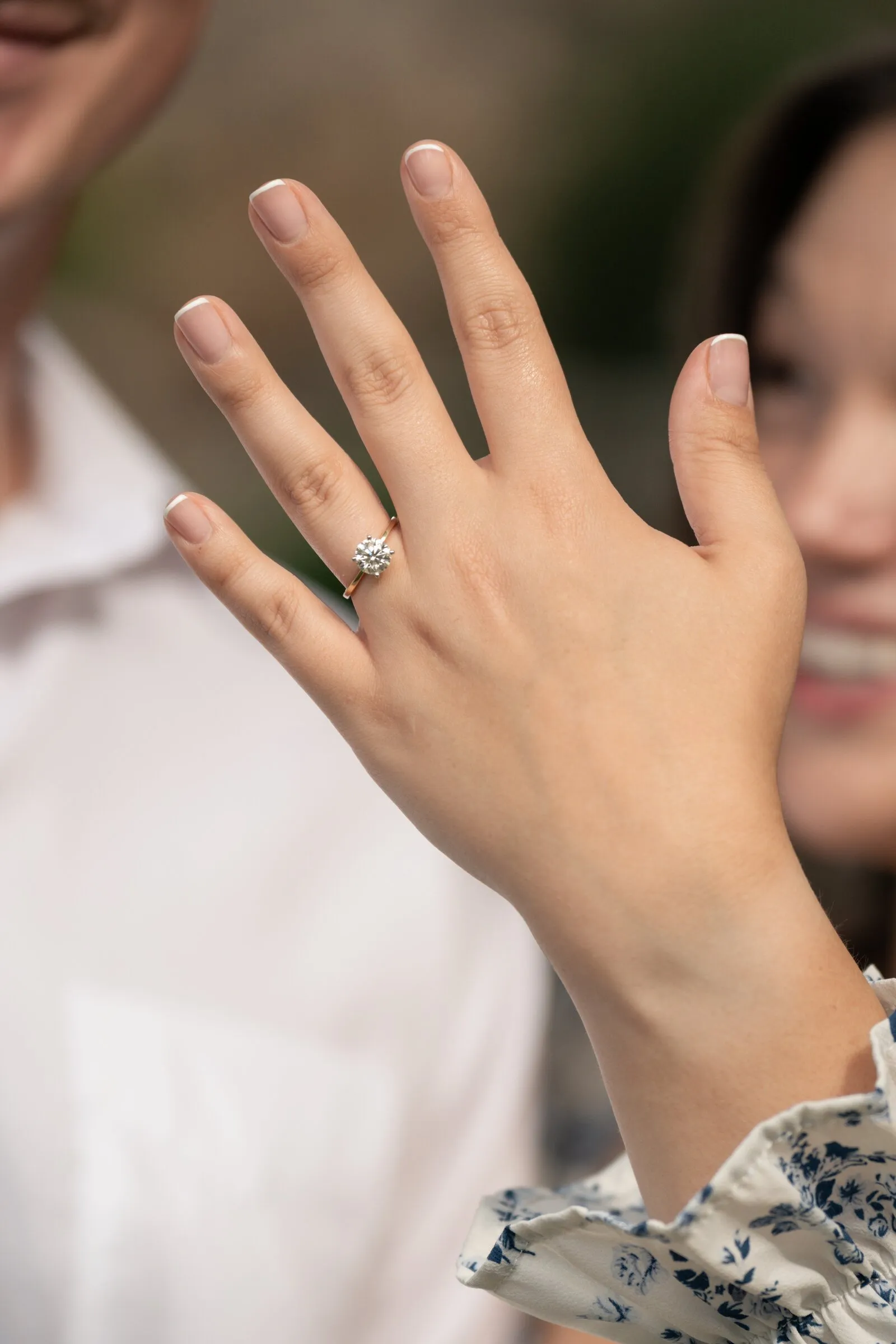 Kayla's hand and ring held up to the camera, her smile softly blurred behind it