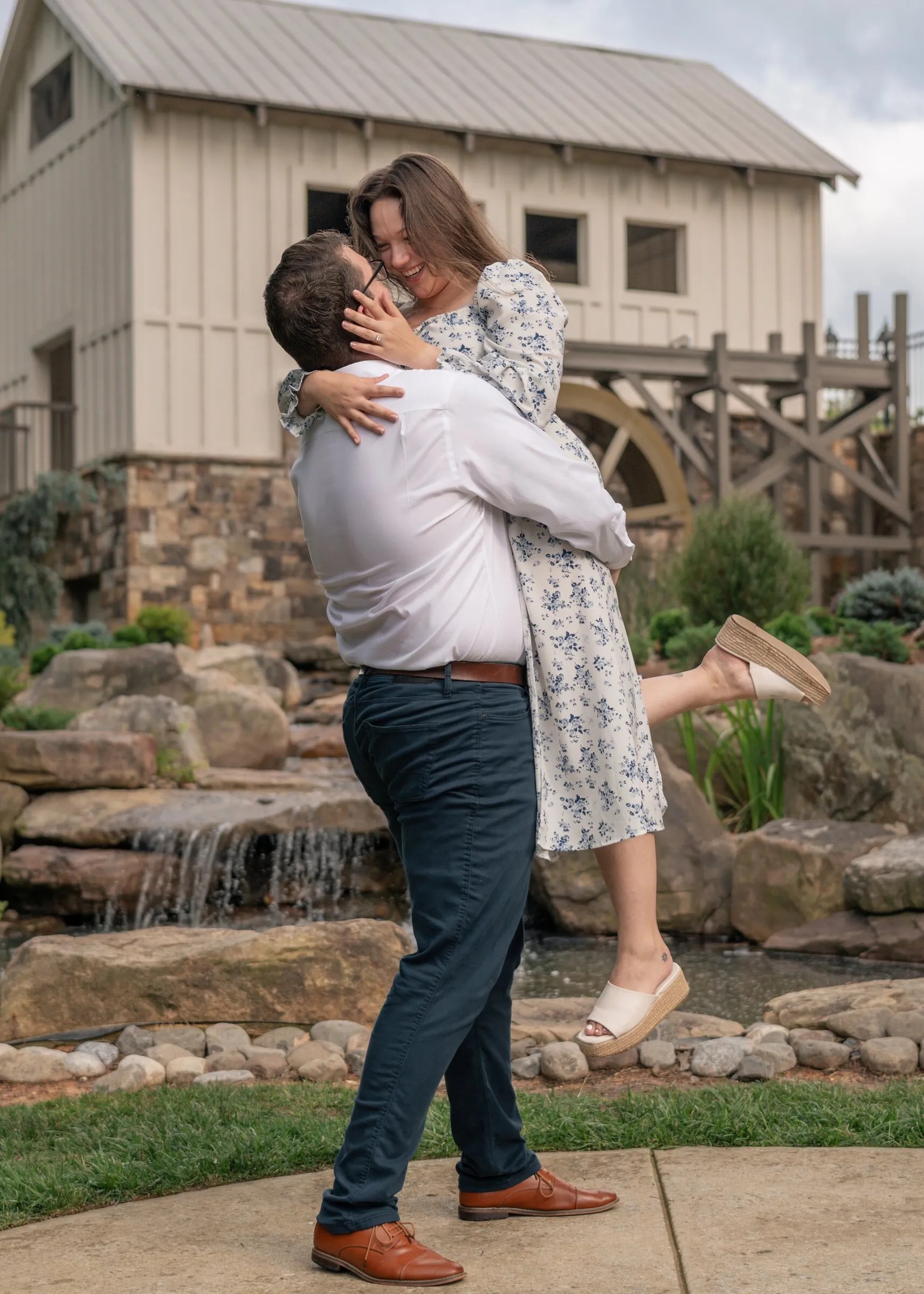 Kayla kicking up one foot as Spencer lifts her in a hug in front of the mill