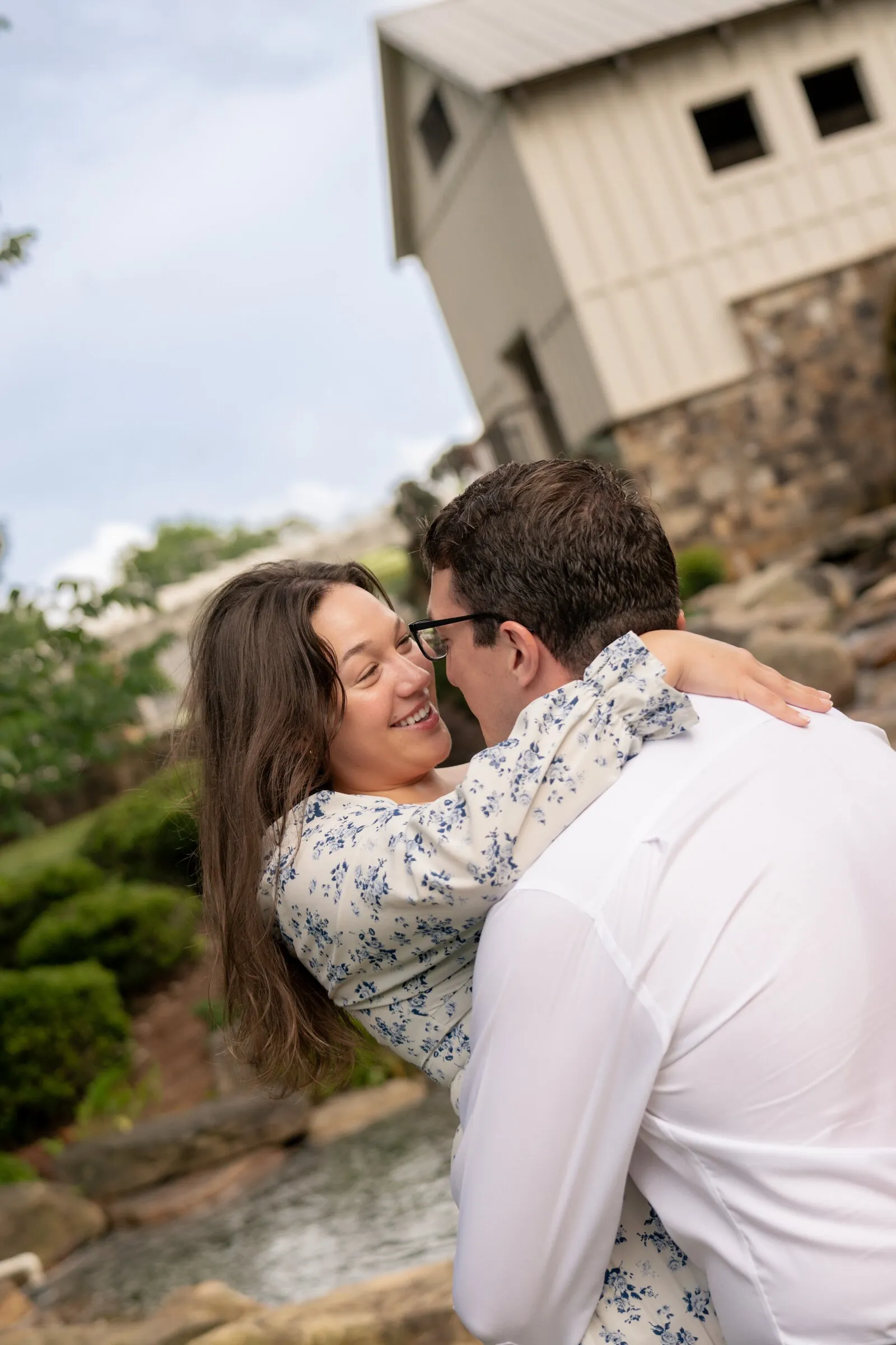 Spencer and Kayla in a tilted embrace beside the mill house, both smiling