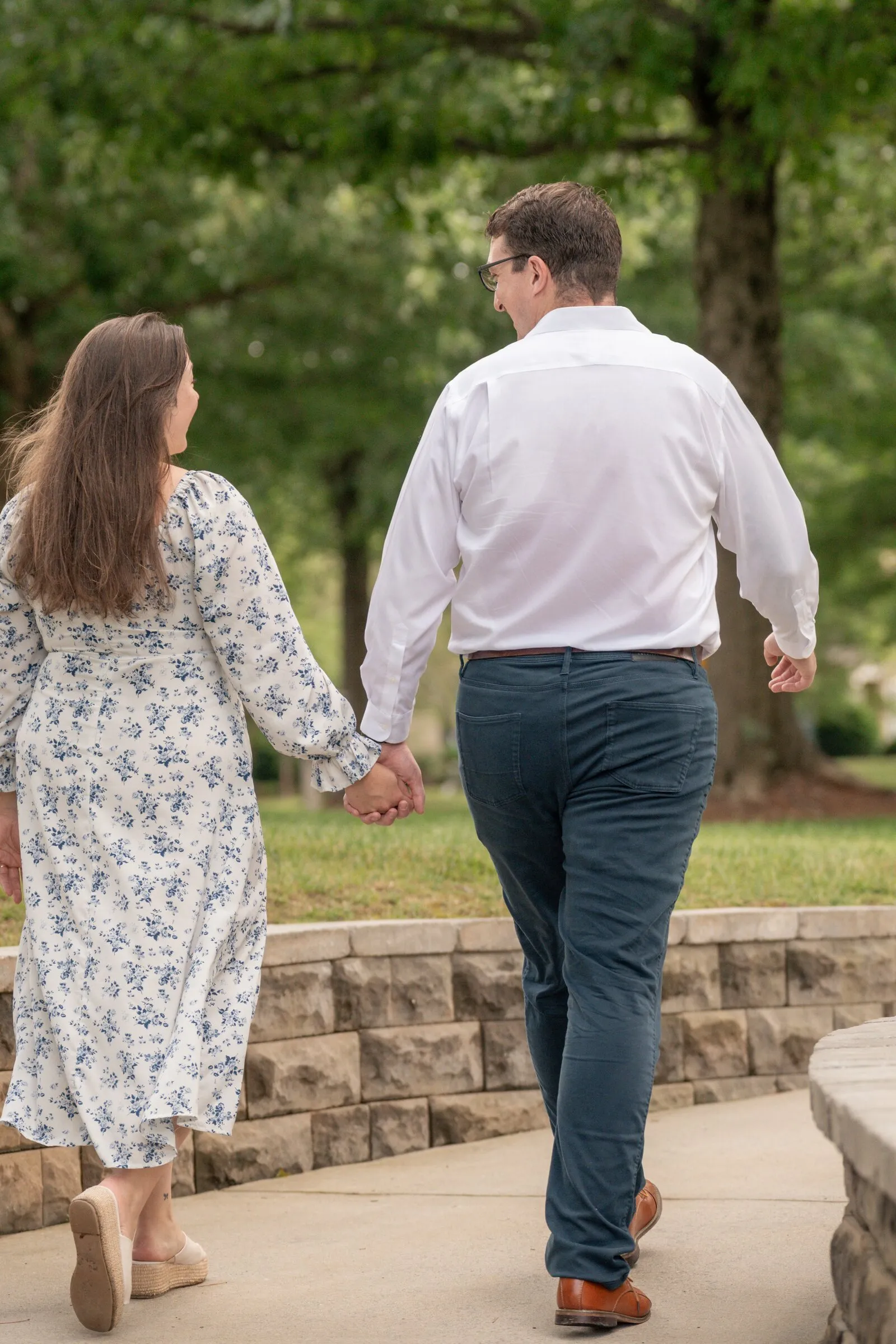 Spencer leading Kayla by the hand along a curved stone wall