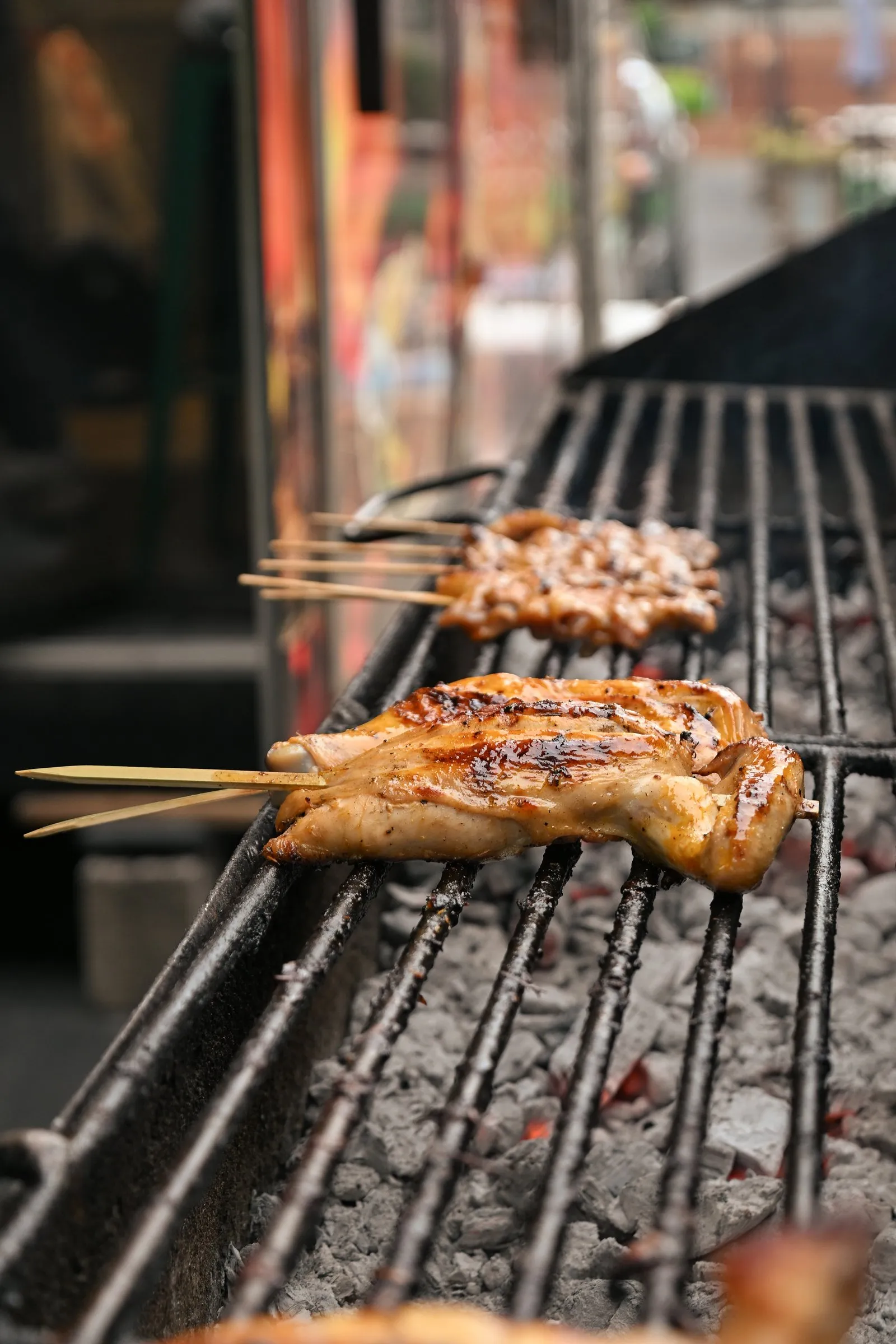 Chicken inasal skewers charring over hot coals on a long open grill