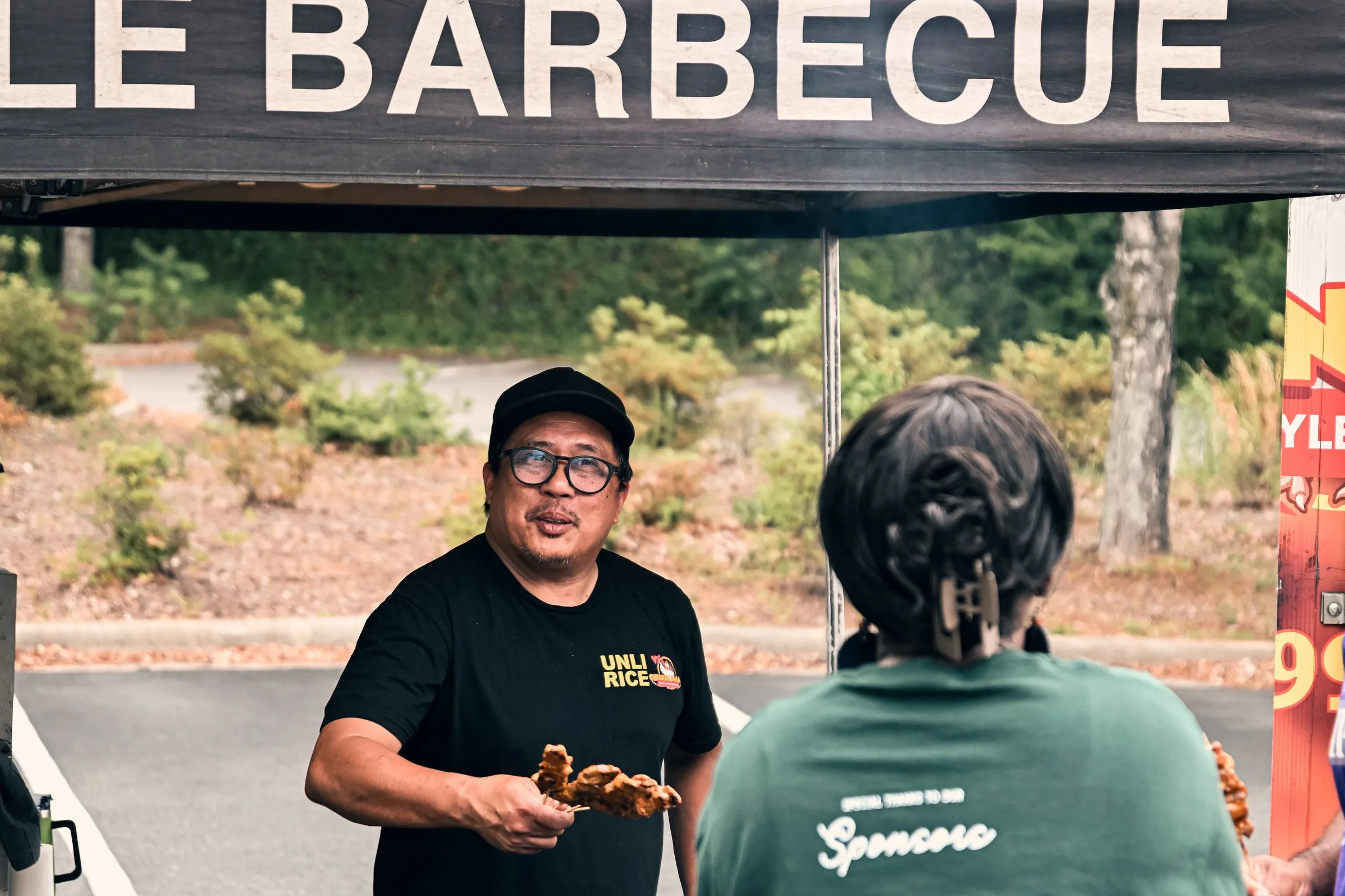 The cook offers a skewer of chicken inasal to a customer at the grill