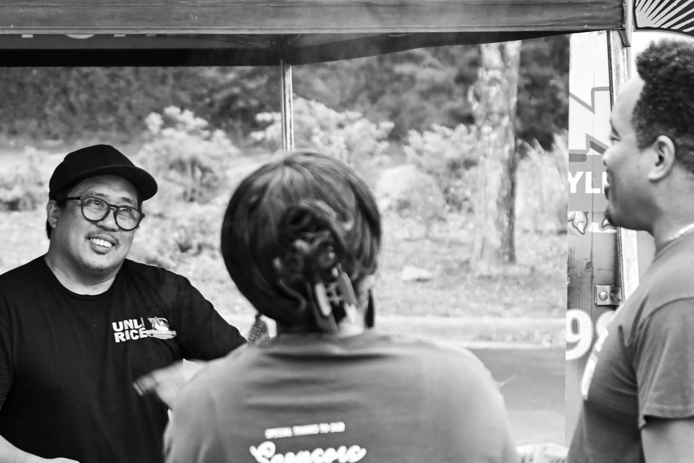Black and white photograph of the cook laughing with customers at the grill