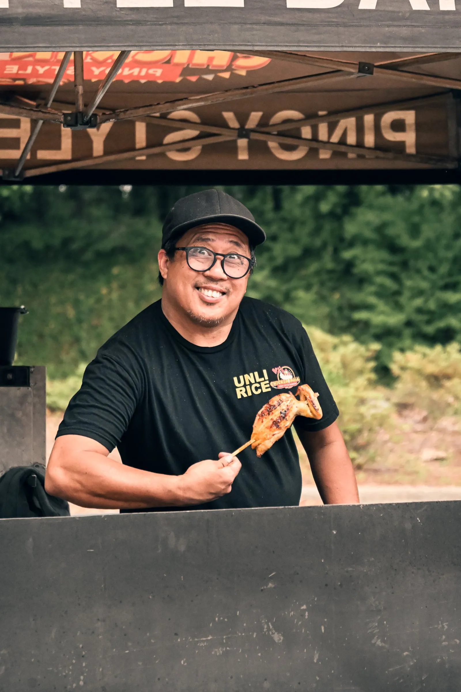 Smiling behind the grill with a skewer of chicken inasal