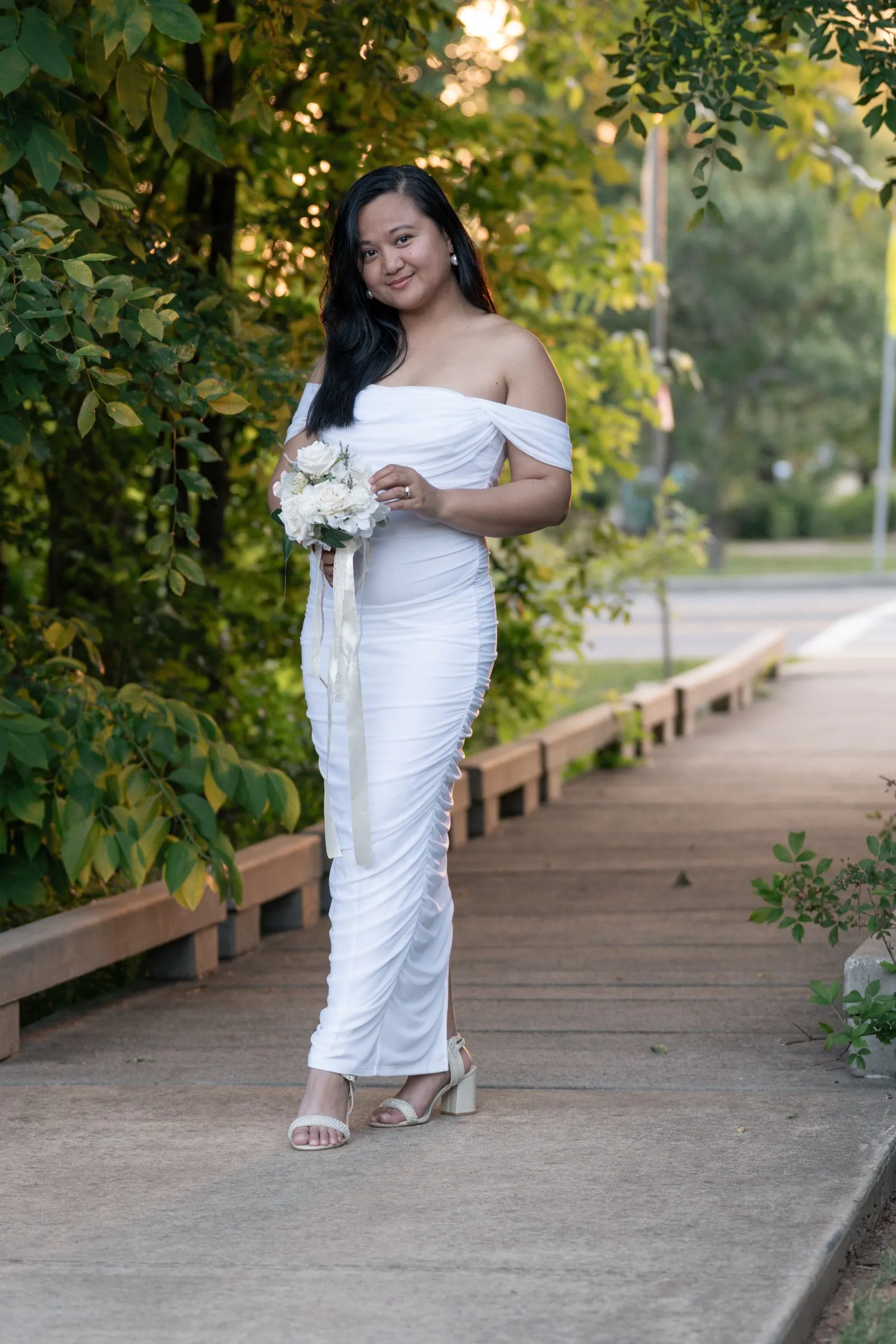 Winnie standing on the boardwalk with her bouquet at her waist, smiling as the evening light catches the leaves