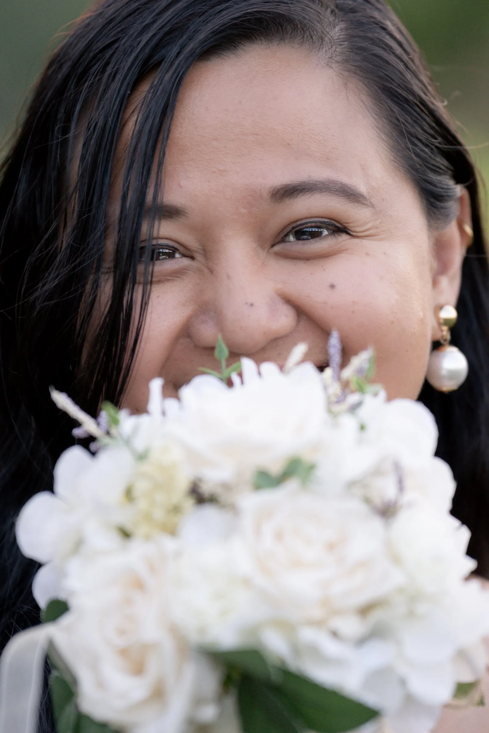 Winnie smiling with her eyes, her face half hidden behind a full bouquet of cream roses and hydrangea