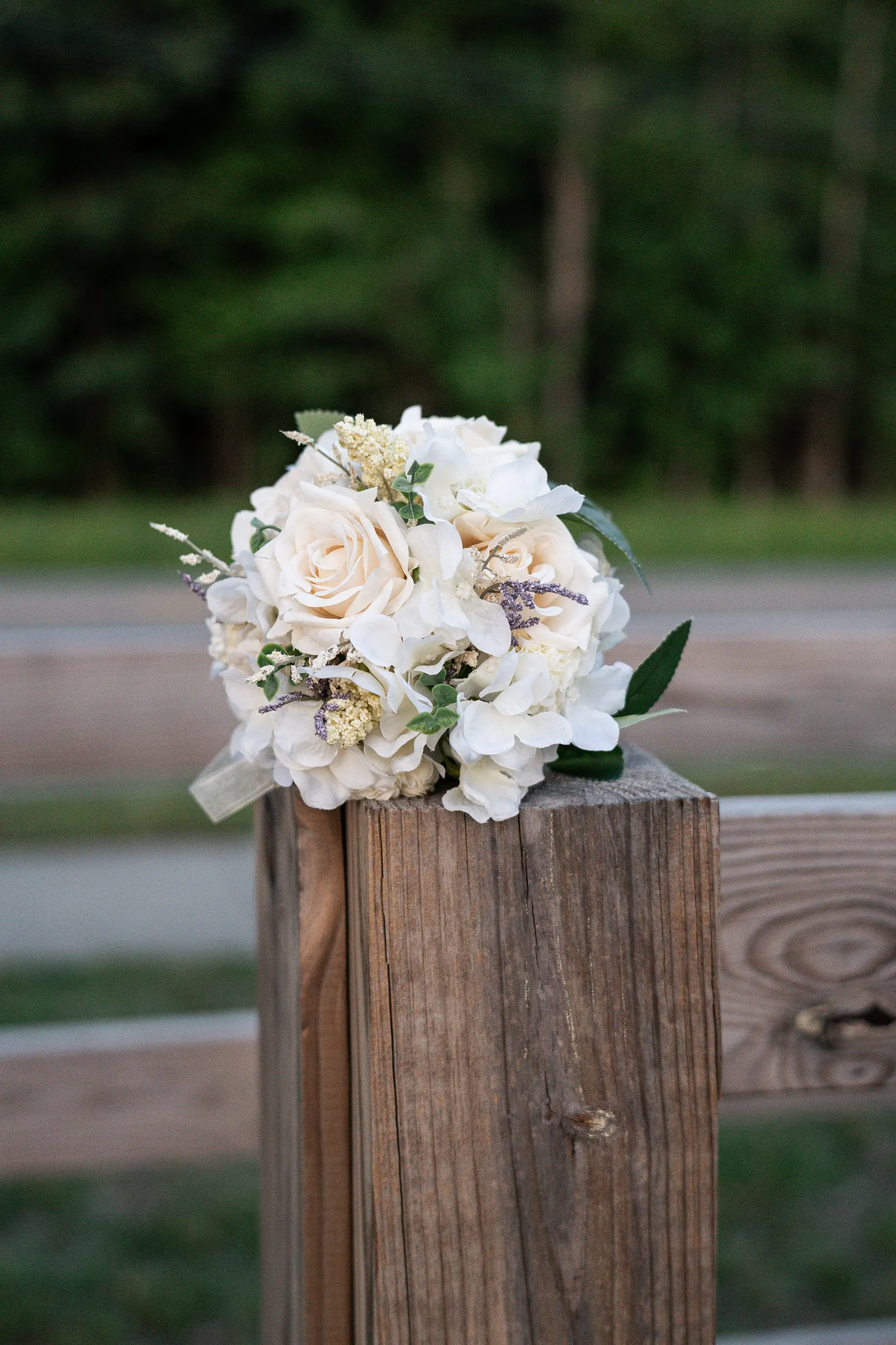 Winnie's bouquet of cream roses and dried flowers resting on top of a weathered wooden fence post
