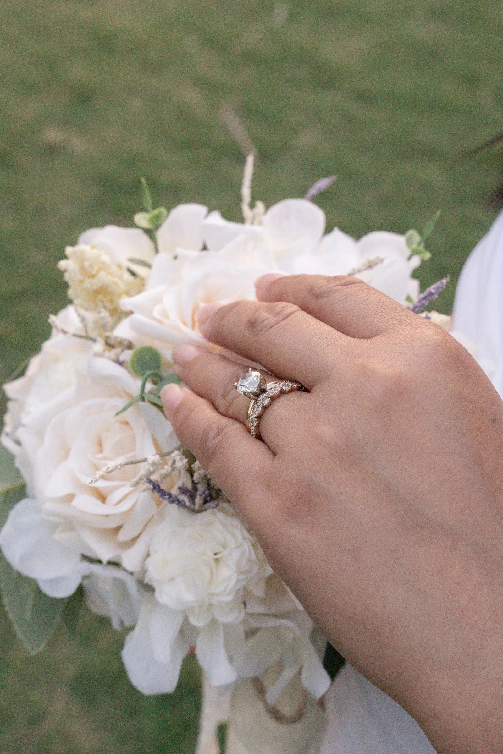Winnie's hand resting on her bouquet of cream roses, her engagement ring and wedding band in focus