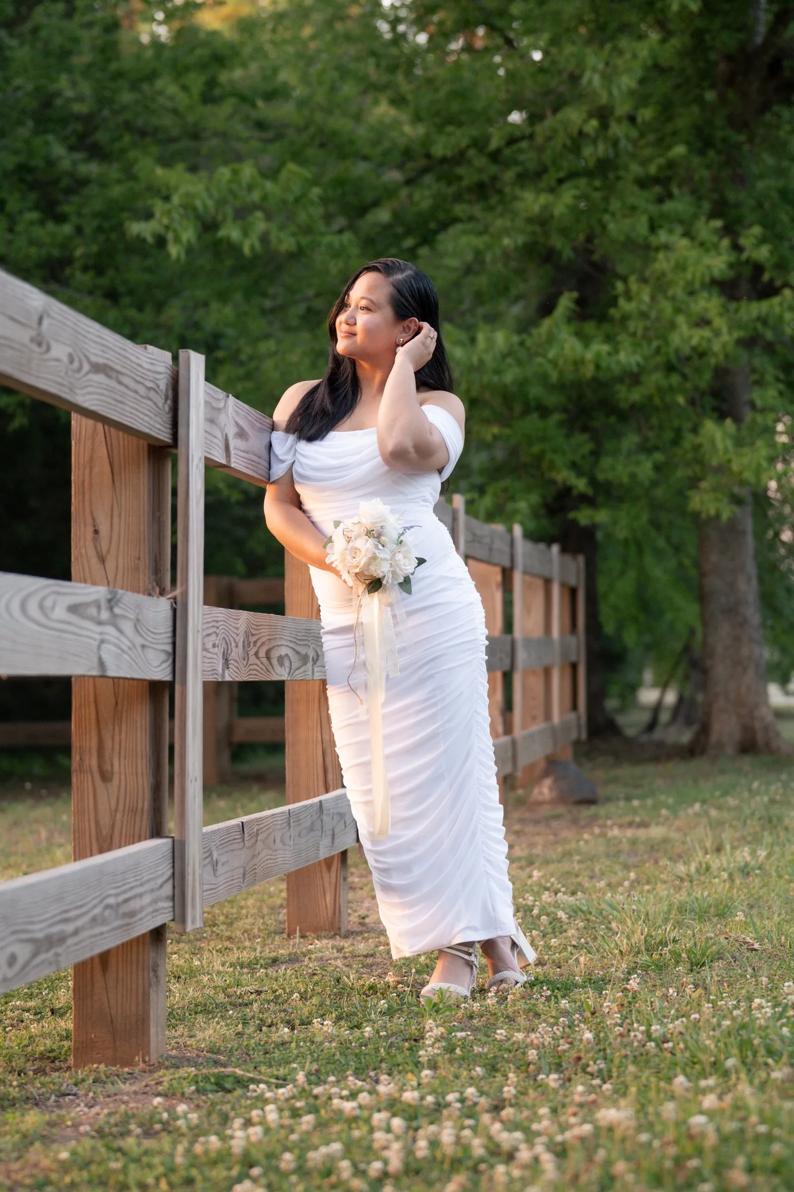 Winnie in her wedding dress leaning against a wooden split rail fence at golden hour in Charlotte, NC