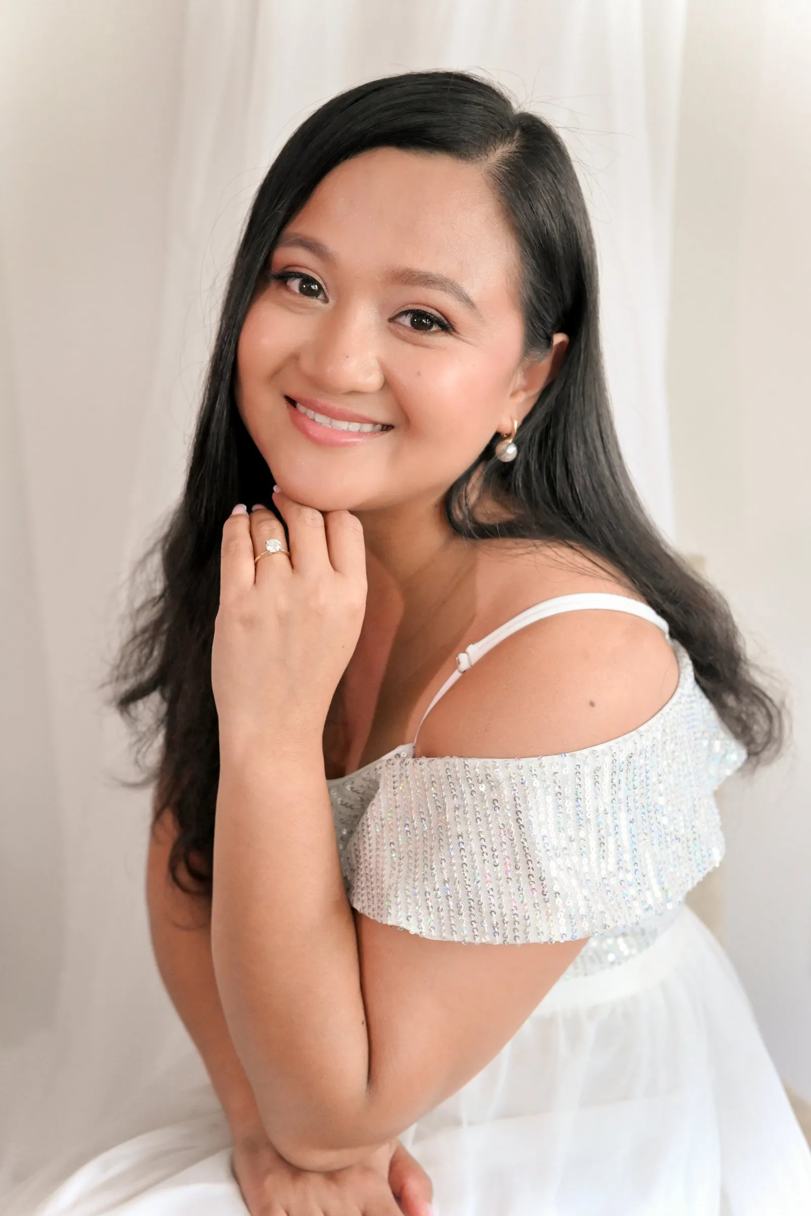 Closer bridal portrait of Winnie smiling softly in her white sequin dress against sheer white curtains before the celebration dinner