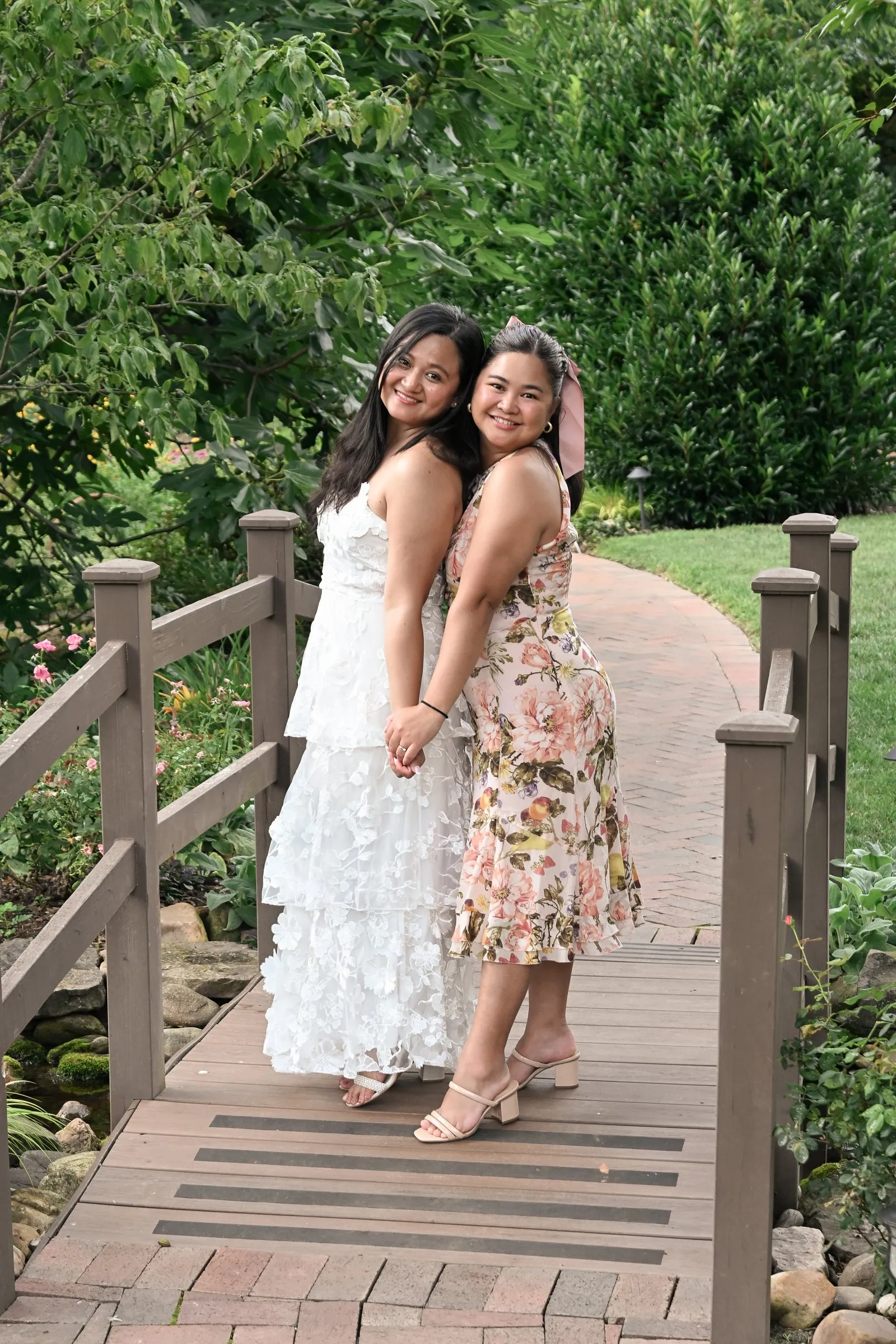 Winnie and her bridesmaid posing back to back, cheek to cheek, on the garden footbridge at Alexander Homestead
