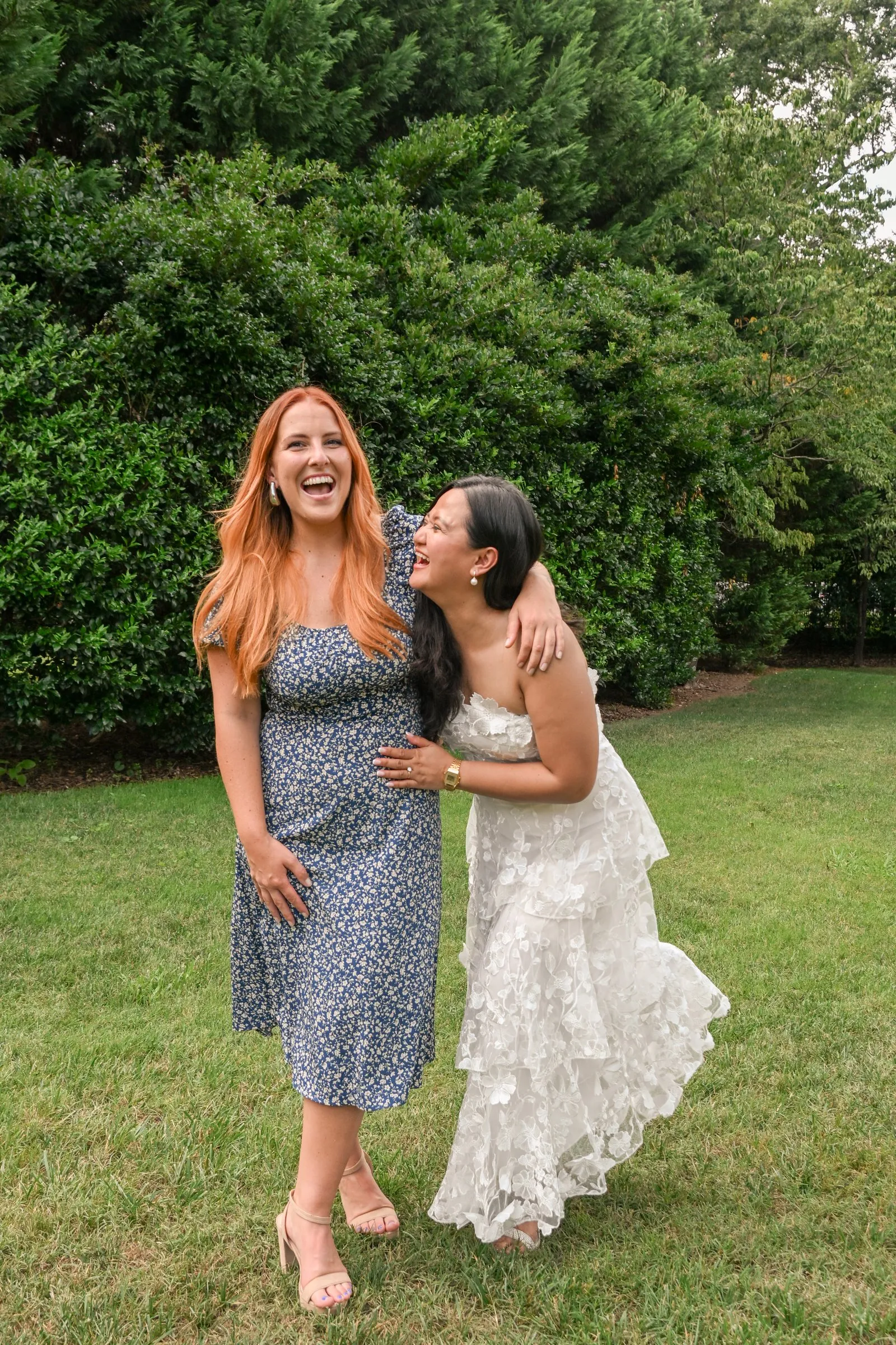 Winnie leaning into her bridesmaid and laughing on the Alexander Homestead lawn the day of the wedding rehearsal