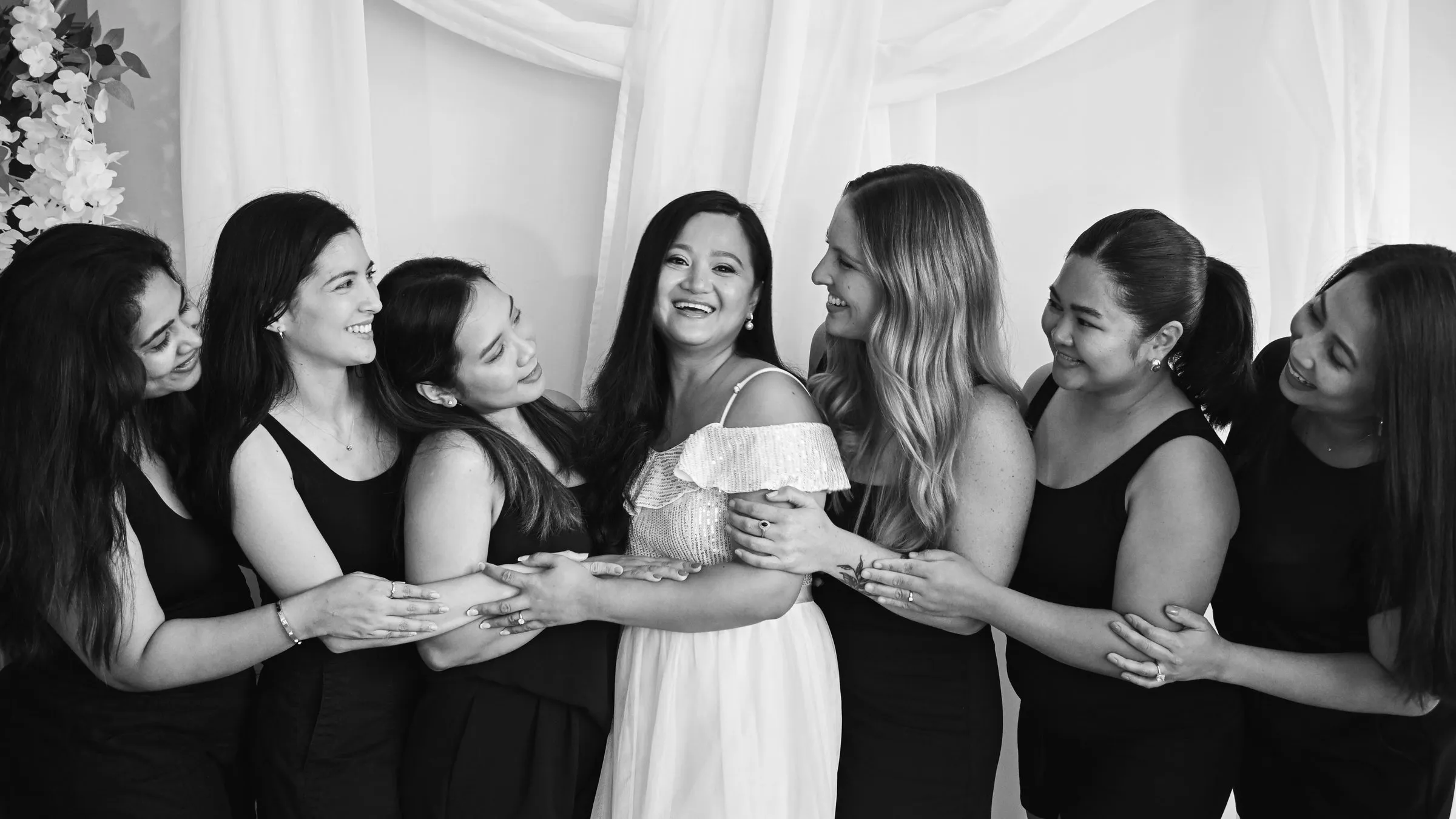 Black and white portrait of Winnie and her bridesmaids, arms linked in a row, smiling at one another before dinner