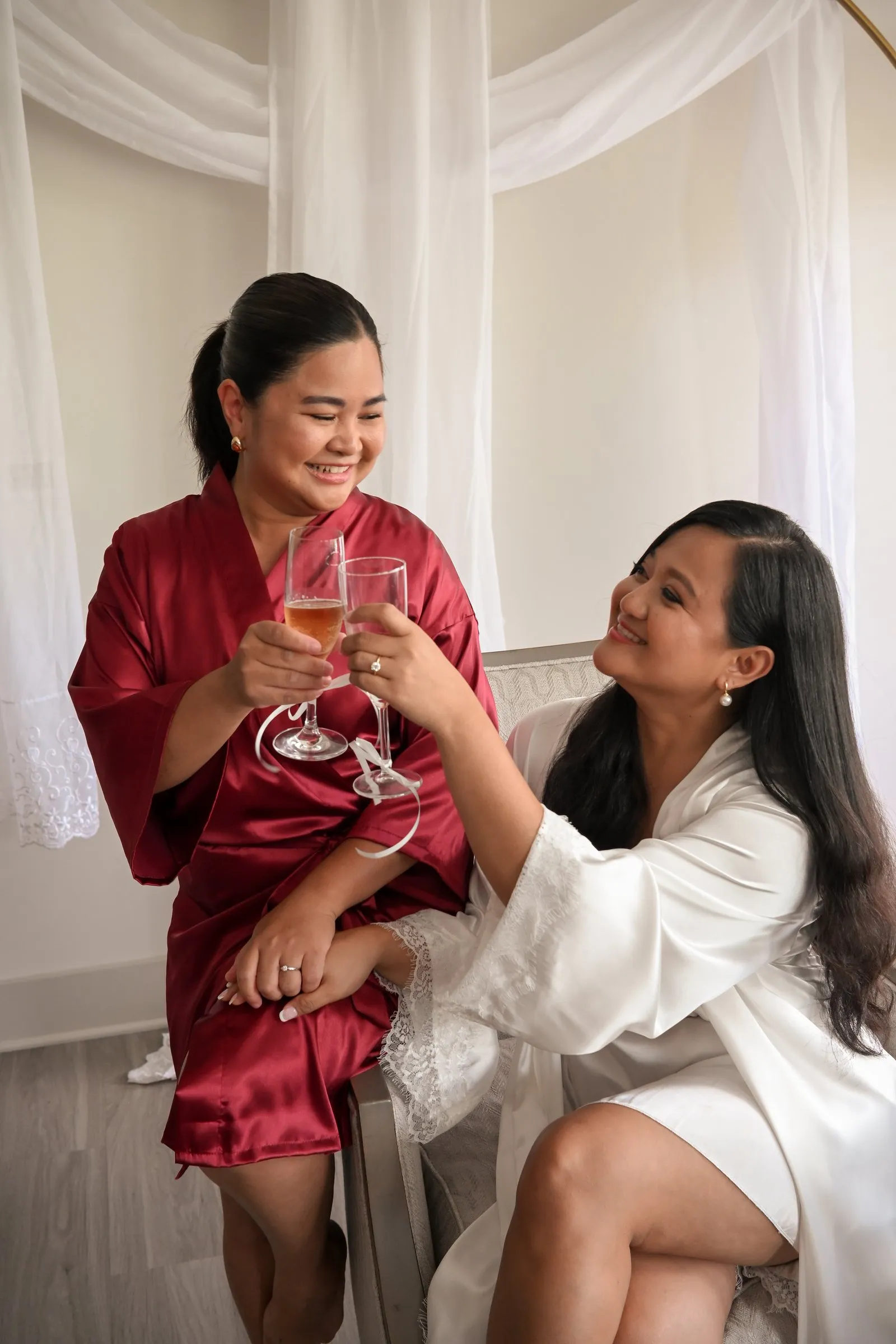 Mathelle in a red satin robe toasting Winnie with champagne as Winnie looks up at her and smiles